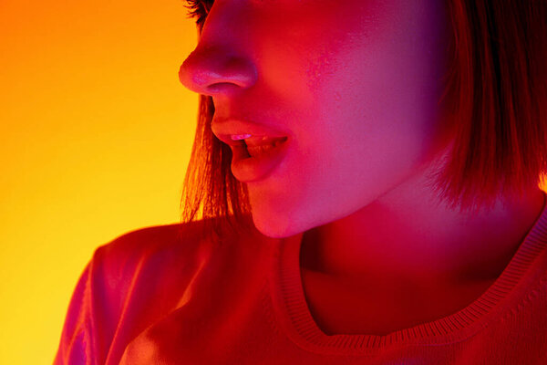 Caucasian womans portrait isolated on orange studio background in multicolored neon light