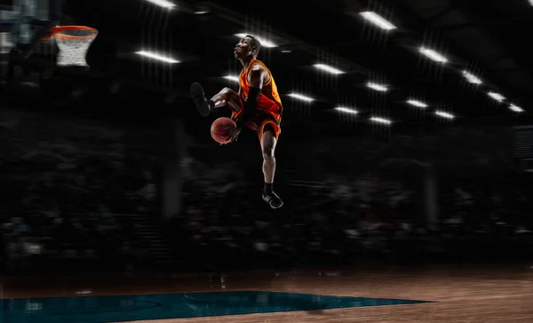 Jugador de baloncesto joven afroamericano en acción y linternas sobre el fondo del gimnasio. Concepto de deporte, movimiento, energía y estilo de vida dinámico y saludable. —  Fotos de Stock