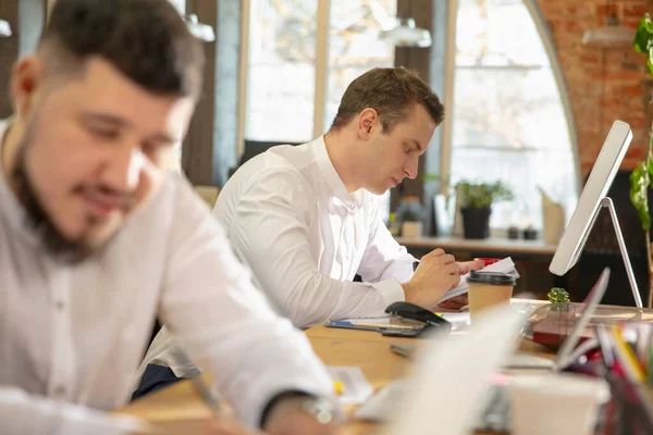 Jóvenes colegas caucásicos trabajando juntos en una oficina utilizando dispositivos y dispositivos modernos — Foto de Stock