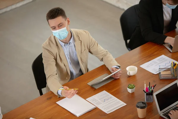 High angle view colleagues working together in face masks during quarantine in a office using modern devices and gadgets during creative meeting — Stock Photo, Image