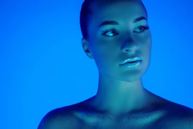 Yakışıklı kadın portresi mavi stüdyo arka planında izole edilmiş neon ışıklı, tek renkli