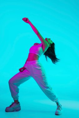 Esmer, güzel kadın portresi mavi stüdyo arka planında çok renkli neon ışıklarla izole edilmiş.