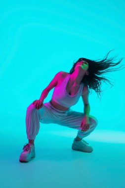 Esmer, güzel kadın portresi mavi stüdyo arka planında çok renkli neon ışıklarla izole edilmiş.