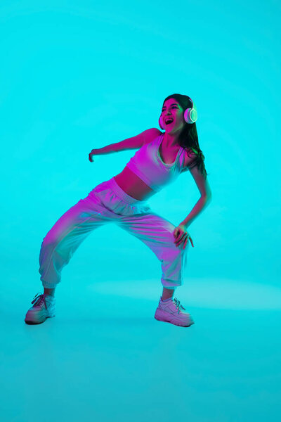 Брюнетка красивый женский портрет изолирован на синем фоне студии в разноцветном неоновом свете. Танцы в наушниках