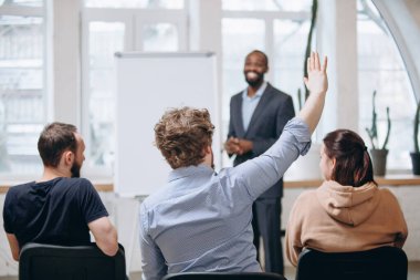 Erkek konuşmacı atölyede sunum yapıyor. Seyirci ya da konferans salonu. Tanınmayan katılımcıların arka görünümü.
