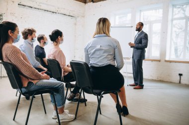 Erkek konuşmacı atölyede sunum yapıyor. Seyirci ya da konferans salonu. Tanınmayan katılımcıların arka görünümü.