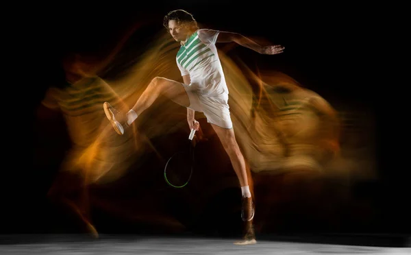 Młody biały profesjonalny sportowiec gra w tenisa na czarny tło w mieszane światło — Zdjęcie stockowe