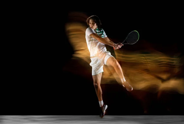 Young caucasian professional sportsman playing tennis on black background in mixed light — Stock Photo, Image