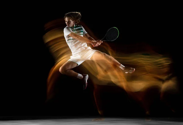 Jovem esportista profissional caucasiano jogando tênis em fundo preto em luz mista — Fotografia de Stock