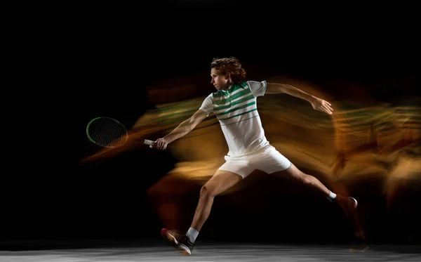 Jovem esportista profissional caucasiano jogando tênis em fundo preto em luz mista — Fotografia de Stock