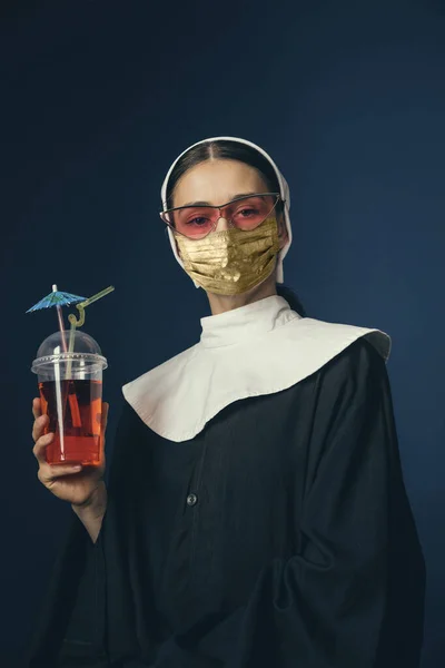 Jovem medieval como freira em roupas vintage e máscara dourada no fundo azul escuro. Conceito de comparação de eras, proteção contra covid — Fotografia de Stock