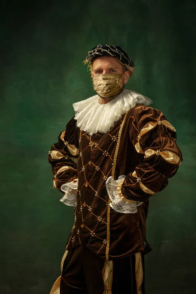 Portrait of medieval young man in vintage clothing and golden face mask standing on dark background. — Stock Photo, Image