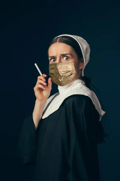 Mittelalterliche junge Frau als Nonne in Vintage-Kleidung und goldener Gesichtsmaske auf dunkelblauem Hintergrund. Konzept des Epochenvergleichs, Schutz vor Kovid — Stockfoto