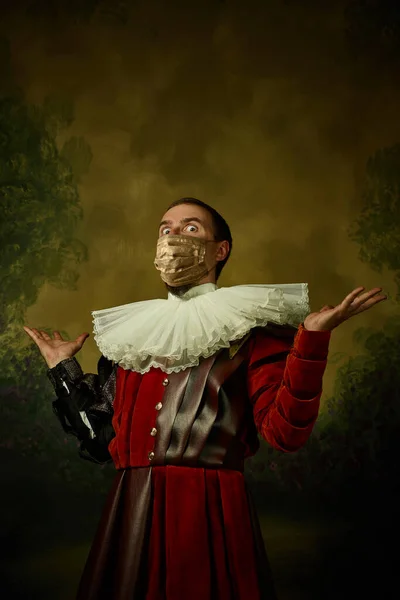 Portrét středověkého mladého muže ve vinobraní oblečení a zlaté masce obličeje stojící na tmavém pozadí. — Stock fotografie