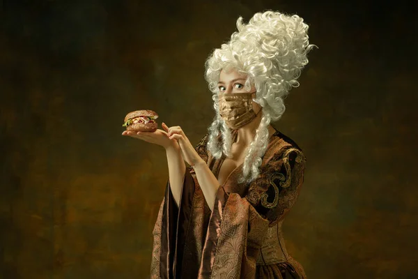 Portræt af middelalderlig ung kvinde i vintage tøj og gylden ansigtsmaske på mørk baggrund. - Stock-foto
