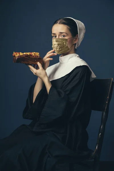 Joven mujer medieval como monja en ropa vintage y máscara dorada sobre fondo azul oscuro. Concepto de comparación de épocas, protección contra el covidio — Foto de Stock