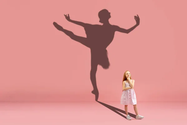 Infância e sonho sobre o futuro grande e famoso. Imagem conceitual com menina e sombra de bailarina fit dançando no fundo rosa coral — Fotografia de Stock