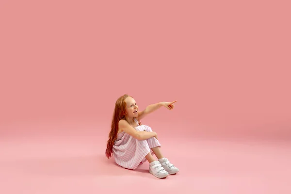 Infância e sonho sobre o futuro grande e famoso. Menina longhair bonita isolado no fundo rosa coral — Fotografia de Stock