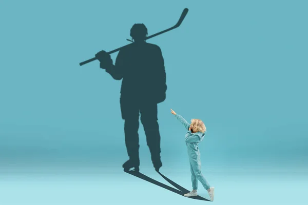 Infancia y sueño sobre el futuro grande y famoso. Imagen conceptual con niño y sombra de jugador de hockey masculino en el fondo azul —  Fotos de Stock