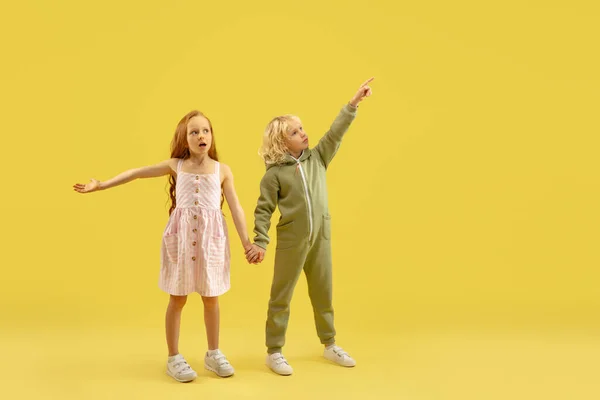 Infancia y sueño sobre el futuro grande y famoso. Niño y niña aislados en el fondo amarillo del estudio — Foto de Stock