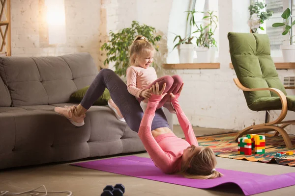 Young woman exercising fitness, aerobic, yoga at home, sporty lifestyle. Getting active with her child playing, home gym.