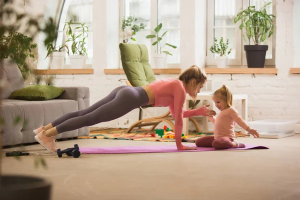 Spor yapan genç bir kadın, aerobik, evde yoga, spor yaşam tarzı. Çocuğu arka planda oynarken aktif hale geliyor.. — Stok fotoğraf