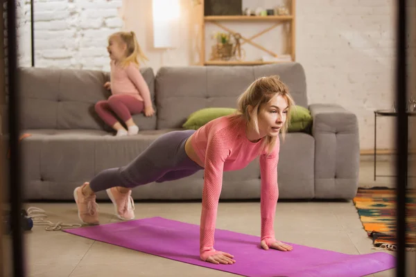 Spor yapan genç bir kadın, aerobik, evde yoga, spor yaşam tarzı. Çocuğu arka planda oynarken aktif hale geliyor.. — Stok fotoğraf