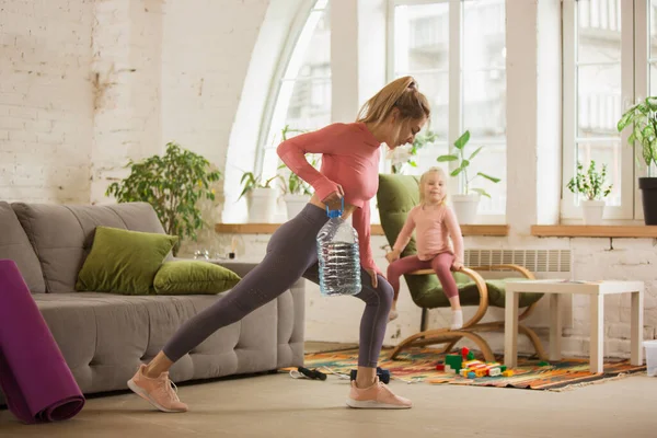 Mujer joven ejercitando fitness, aeróbico, yoga en casa, estilo de vida deportivo. Ponerse activa con su hijo jugando, gimnasio en casa. — Foto de Stock