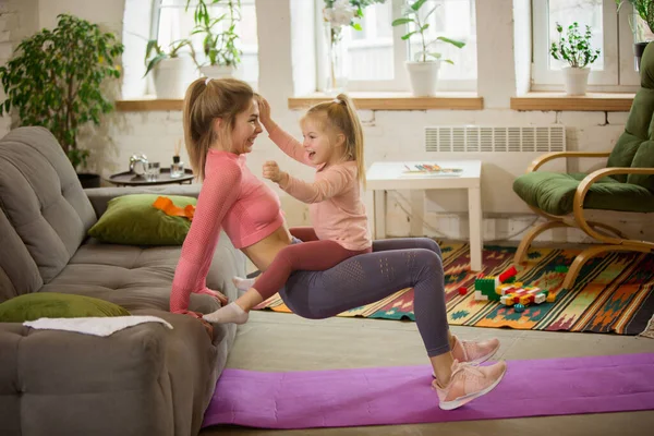 Mladá žena cvičit fitness, aerobic, jóga doma, sportovní životní styl. Aktivní s její dítě hrát, domácí tělocvična. — Stock fotografie