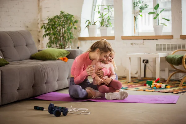 Mladá žena cvičit fitness, aerobic, jóga doma, sportovní životní styl. Aktivní, když dítě, dcera si s ní hraje, domácí tělocvična. — Stock fotografie