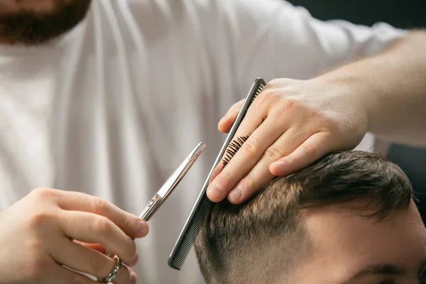 Cerca de las manos del maestro barbero, estilista hace el peinado a chico, joven. Ocupación profesional, concepto de belleza masculino — Foto de Stock