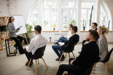 Kadın konuşmacı atölyede sunum yapıyor. Seyirci ya da konferans salonu. Tanınmayan katılımcıların kenar görünümü.