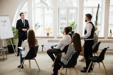 Erkek konuşmacı atölyede sunum yapıyor. Seyirci ya da konferans salonu. Tanınmayan katılımcıların arka görünümü.