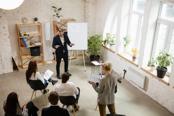 Mužský řečník přednáší v hale na workshopu. Audience nebo konferenční sál. Vysoký úhel neznámých účastníků. — Stock fotografie