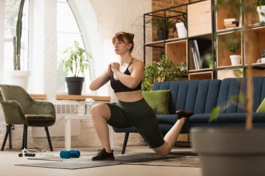 Spor yapan genç bir kadın, aerobik, evde yoga, spor yaşam tarzı. Tecrit sırasında aktif hale gelip karantinaya alınıyor. Evde spor salonu.