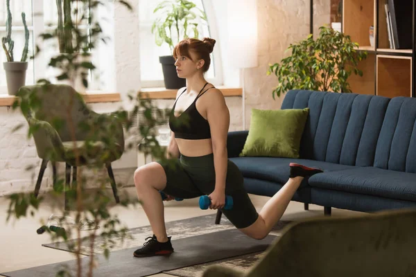 Mujer joven ejercitando fitness, aeróbico, yoga en casa, estilo de vida deportivo. Activarse durante el encierro, cuarentena. Gimnasio. — Foto de Stock