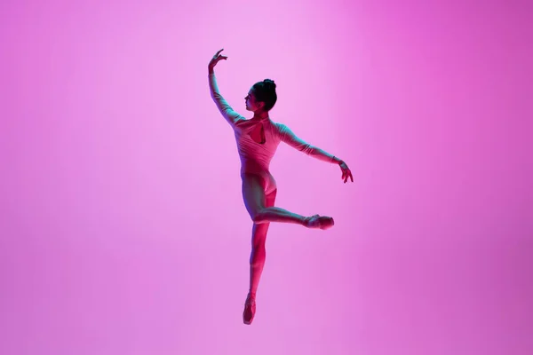 Młoda i pełna wdzięku tancerka baletowa odizolowana na różowym tle studia w neonowym świetle. Sztuka, ruch, działanie, elastyczność, koncepcja inspiracji. — Zdjęcie stockowe