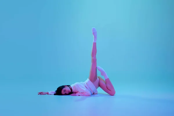 Młoda i pełna wdzięku tancerka baletowa odizolowana na niebieskim tle studia w neonowym świetle. Sztuka, ruch, działanie, elastyczność, koncepcja inspiracji. — Zdjęcie stockowe
