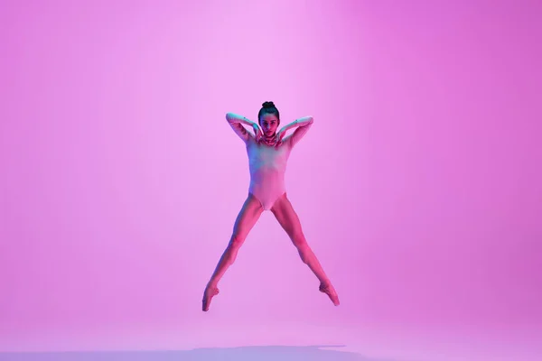 Młoda i pełna wdzięku tancerka baletowa odizolowana na różowym tle studia w neonowym świetle. Sztuka, ruch, działanie, elastyczność, koncepcja inspiracji. — Zdjęcie stockowe