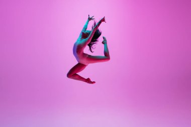 Genç ve zarif balerin pembe stüdyo arka planında neon ışıkta izole edilmiş. Sanat, hareket, eylem, esneklik, ilham kavramı.