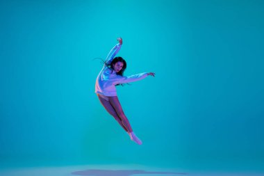 Genç ve zarif balerin mavi stüdyo arka planında neon ışıklarıyla izole edilmiş. Sanat, hareket, eylem, esneklik, ilham kavramı.