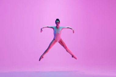 Genç ve zarif balerin pembe stüdyo arka planında neon ışıkta izole edilmiş. Sanat, hareket, eylem, esneklik, ilham kavramı.