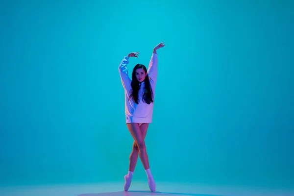 Joven y elegante bailarina de ballet aislada sobre fondo de estudio azul en luz de neón. Arte, movimiento, acción, flexibilidad, concepto de inspiración. — Foto de Stock