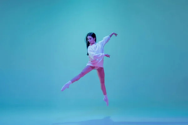 Joven y elegante bailarina de ballet aislada sobre fondo de estudio azul en luz de neón. Arte, movimiento, acción, flexibilidad, concepto de inspiración. — Foto de Stock