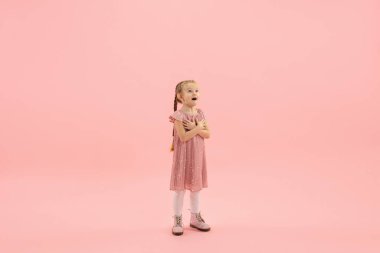 Çocukluk ve büyük ve ünlü bir gelecek hayal etmek. Mercan pembe arka planda izole edilmiş güzel uzun saçlı kız.