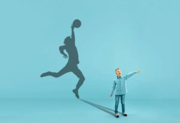 Kindheit und Traum von einer großen und berühmten Zukunft. Konzeptbild mit Junge und Schatten eines fitten männlichen Basketballspielers auf blauem Hintergrund — Stockfoto
