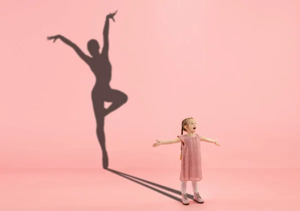 Infancia y sueño sobre el futuro grande y famoso. Imagen conceptual con chica y sombra de la bailarina de ballet en forma sobre fondo rosa coral — Foto de Stock