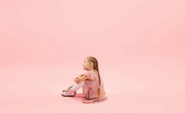 Infância e sonho sobre o futuro grande e famoso. Menina longhair bonita isolado no fundo rosa coral — Fotografia de Stock