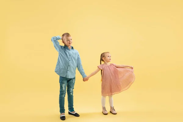 Infancia y sueño sobre el futuro grande y famoso. Niño y niña aislados en el fondo amarillo del estudio — Foto de Stock