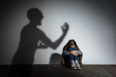 Aile içi şiddet, istismar. Korkmuş küçük beyaz kız, beyaz duvarın yanında oturan kızgın babaların gölgesi altında.